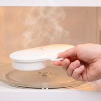 White dual-cavity egg steamer held by its handle inside a microwave