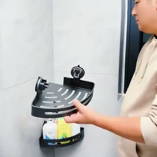 Person holding a gunmetal triangular shower caddy with paired circular suction mounts beside a tiled shower corner