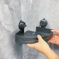 Hands fitting a gunmetal triangular shower caddy beneath two circular suction mounts in a tiled corner