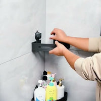 Gunmetal triangular shower caddy being positioned in a white tiled corner above a second caddy holding bottles