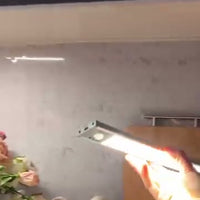 A hand holds a lit white light bar in a kitchen setting.
