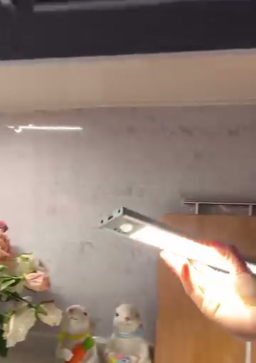 A hand holds a lit white light bar in a kitchen setting.
