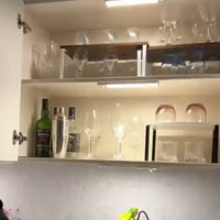 An open kitchen cabinet lit by two white light bars, with glassware and pantry items inside.