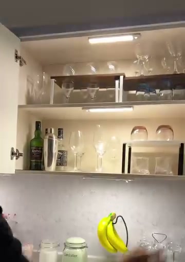An open kitchen cabinet lit by two white light bars, with glassware and pantry items inside.