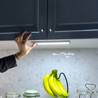 A hand positions one glowing light bar beneath dark kitchen cabinets, with the full bar visible.