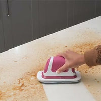 A pink and white flat scrubber moves across a crumb-covered white countertop.