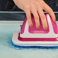 A hand guides the flat scrubber across a blue-tinted wet surface.