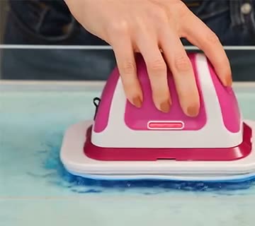 A hand guides the flat scrubber across a blue-tinted wet surface.