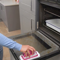 A person uses the flat scrubber on an open oven door.