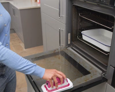 A person uses the flat scrubber on an open oven door.