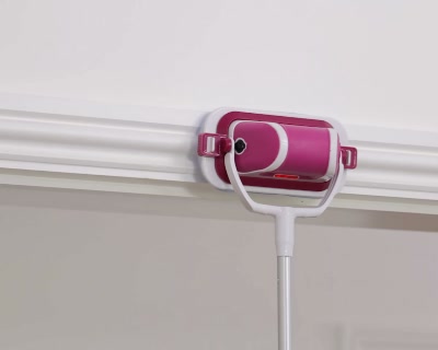 Pink-and-white flat scrubber on an extension pole reaching a high wall edge beside white cornice trim.