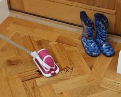 A flat scrubber on an extension pole cleans a wood floor near a cabinet.